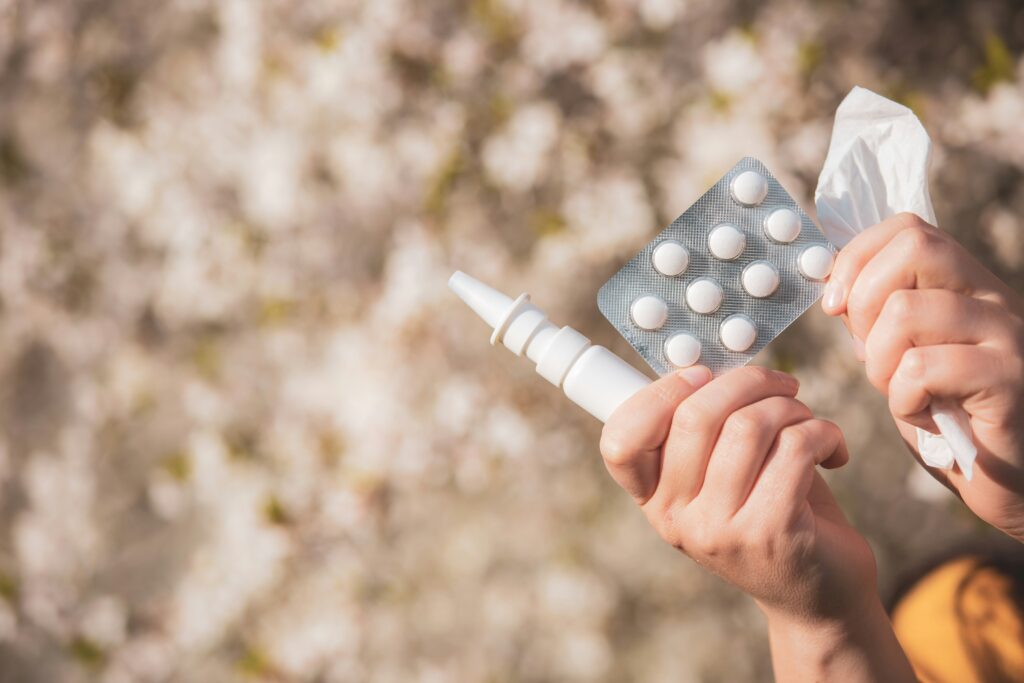 Bild einer Hand die Nasenspray, Allergietabletten und Taschentücher hält