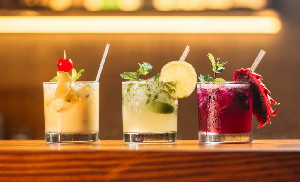 Drei bunte Cocktails auf einem Tresen. Regelmäßiger Alkoholkonsum ist ein gesicherter Risikofaktor für verschiedene Krebserkrankungen.