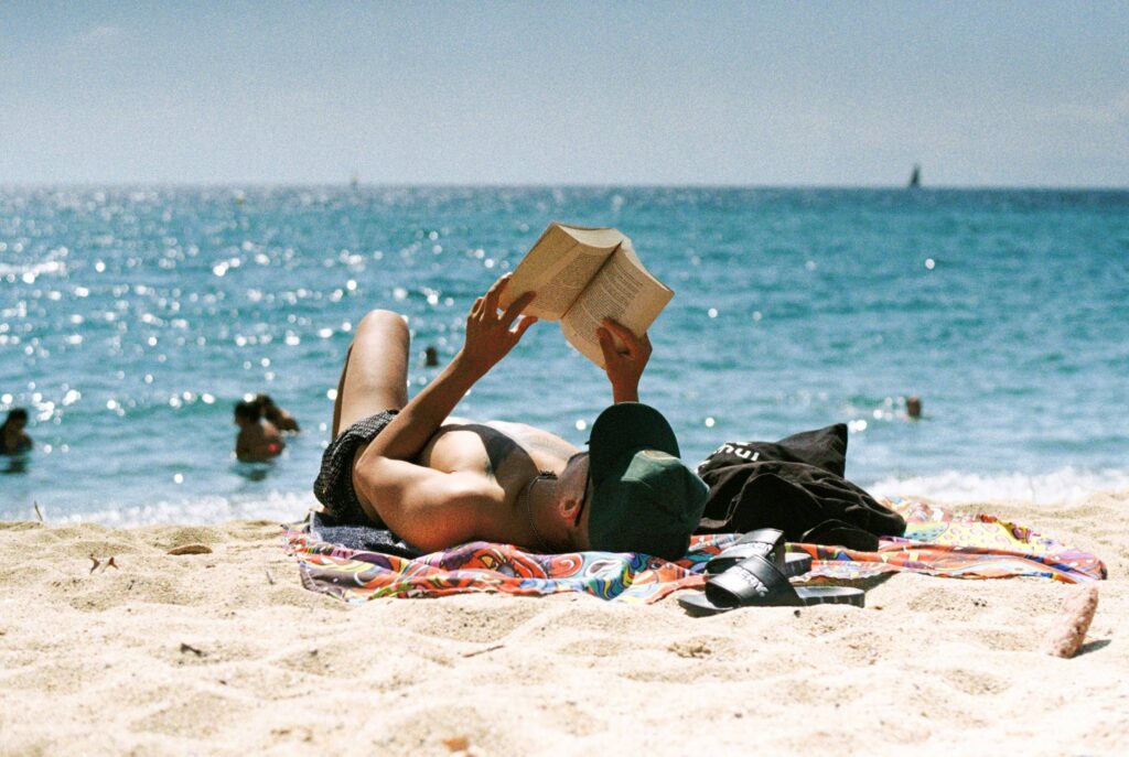 Ein Mann liegt am Strand in der Sonne und liest ein Buch. Intensive UV-Strahlung erhöht das Hautkrebsrisiko drastisch.
